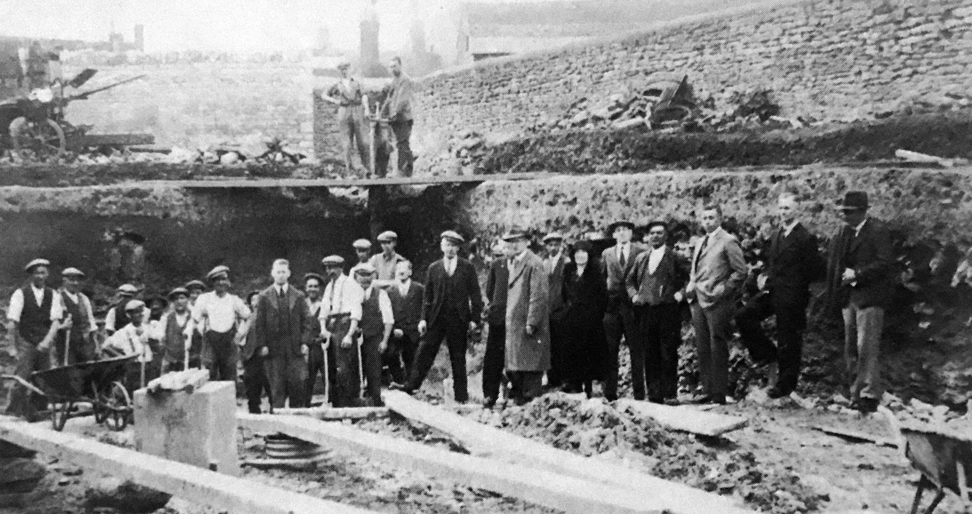 Workmen and members of the pool committee during construction. The people featured include, from the left, Mr H.T. Smith, council surveyor, standing between two workmen; in the centre is Mr Albert Lambourne, chairman of the committee, with his foot on a piece of timber; next to him is Mr Morley Smith, baker and councillor; in front of him stands Mr J.T. Mountain, chemist, wearing a topcoat; and third from the right, with his hands in his pockets, is Mr J.L. Howson, headmaster of Bicester County School.